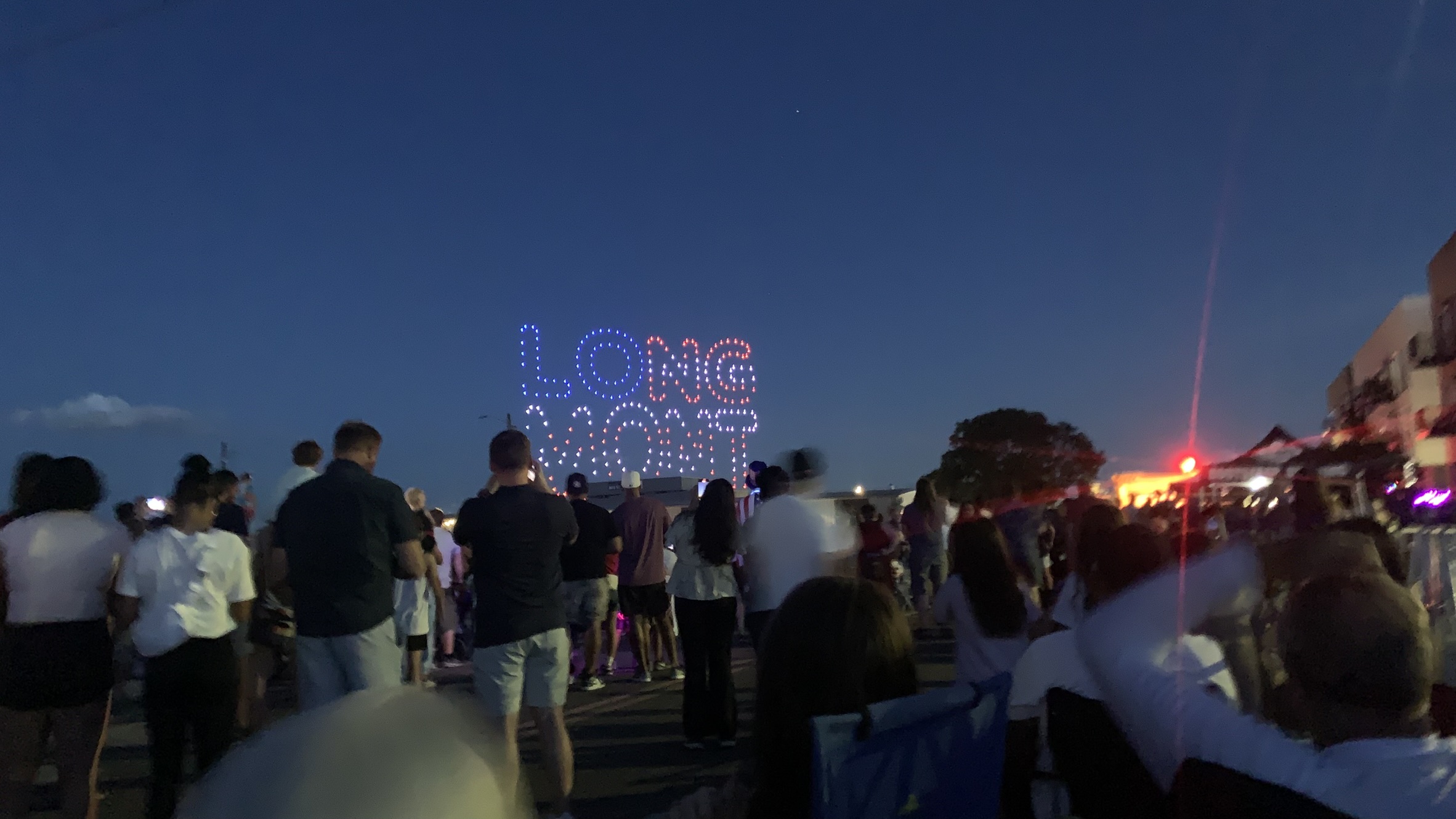 Community members enjoy a July 4, 2025 drone performance created by students with the Innovation Center of St Vrain Valley School District Drone Performance Team. The word "Longmont" lights up the sky in the form of a rectangle colored red, white, and blue to resemble the US flag.