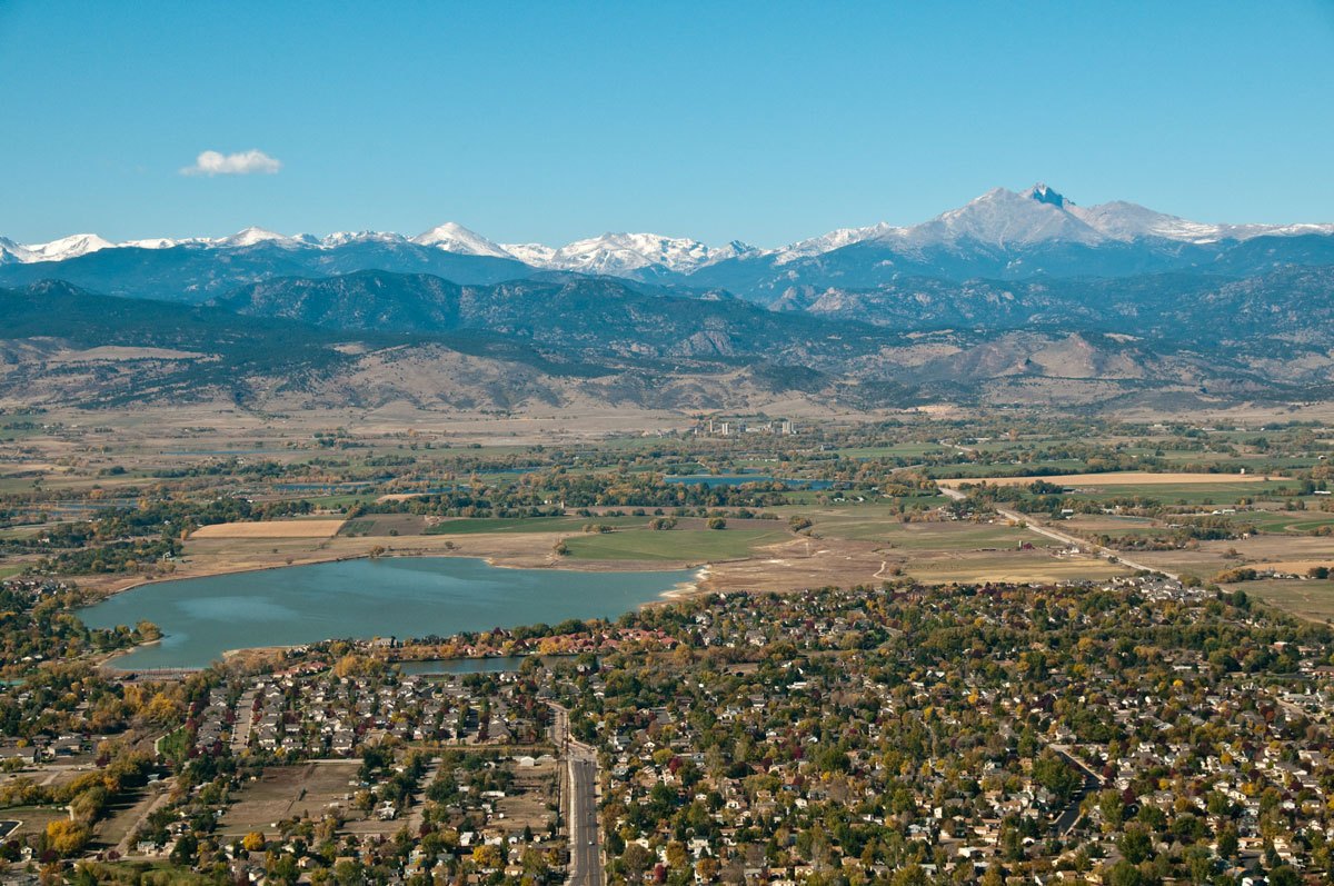 Aerial photo of homes and trees in the foreground with mountains and blue sky in the background.