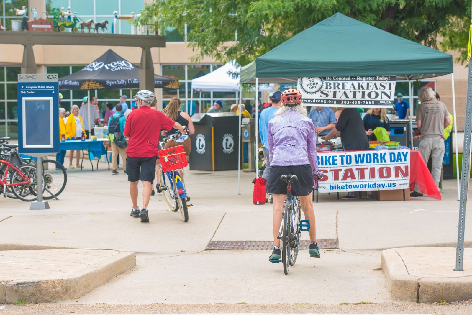 cyclists ride up to a Bike to Work Day food station outside under a tent