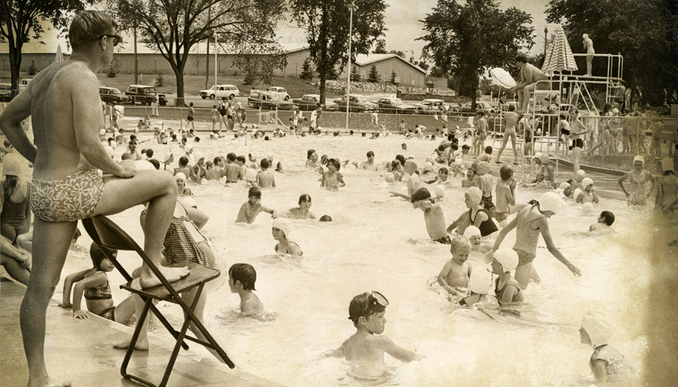 Black and white photo of Sunset Swimming Pool full of kids. Caption: Pool manager Reggie Batt Jr. Surveys the shallow end of Sunset Swimming Pool Friday in the first day of the regular season of swimming. Batt estimated the crowd in the pool at 700, a few short of the maximum allowable. The pool will remain open until Labor Day with registration for Red Cross swimming lessons being made at the Longmont Recreation Department at 700 Longs Peak Ave. Published in the Times-Call on June 10, 1972.