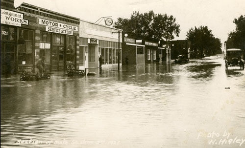 Black and white print of flood on Main St. 1921. Sign on one building reads "Longmont Works" only partly visible. Another sign reads "Motor Cycle Service Station". Main buildings are: Buick (523 Main) Service, Boise Payette Lumber, Motorcycle shop. Terry Lake flood.