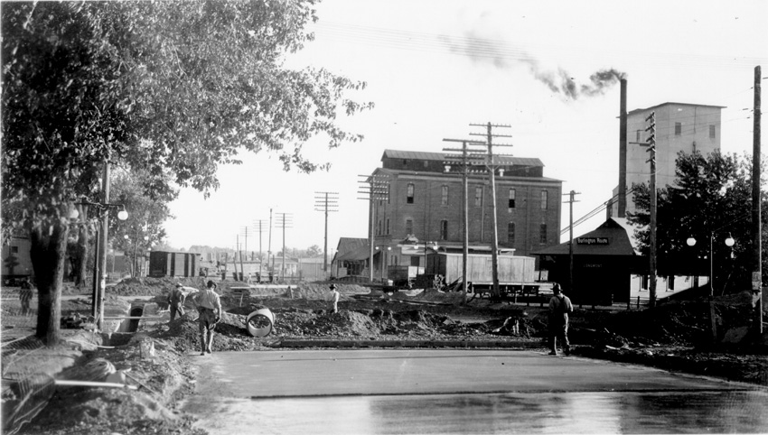 Black and white glossy print showing street paving. Farmers Milling and Elevator in background. Row of trees left side of photo. On back in both pencil and ink, "Farmers Milling & Elevator paving Streets, So. Main."