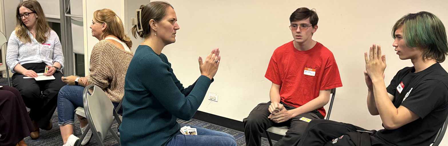 group of people sitting and practicing ASL indoors.