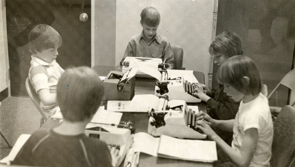 Black and white photo of five children seated at typewriters around a table taking the Type-It classes at Longmont Estates Elementary. Published in the Times-Call on May 10, 1977.