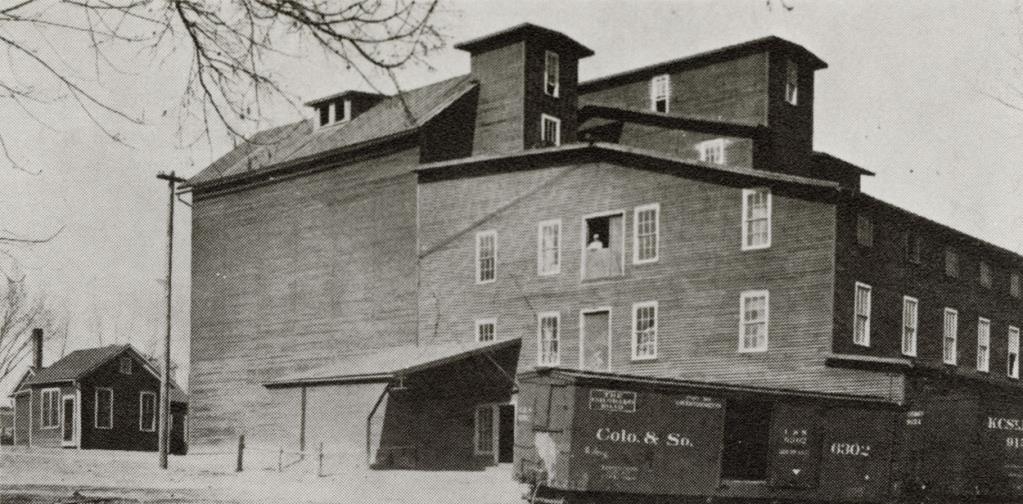 black and white photograph of large mill with "Colo. & So." boxcar in front. Written on back in blue ink "Denio Mill, Old Mill Park