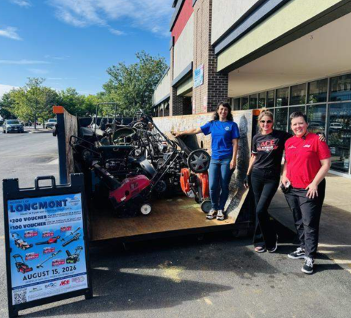 Three people standing in a parking lot next to a truck full of lawn mowers. 