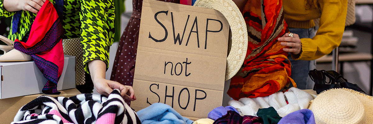 carboard sign that reads "swap not shop" with people going through clothes on a table