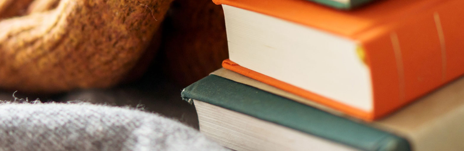A stack of books laying next to a cozy knitted white blanket
