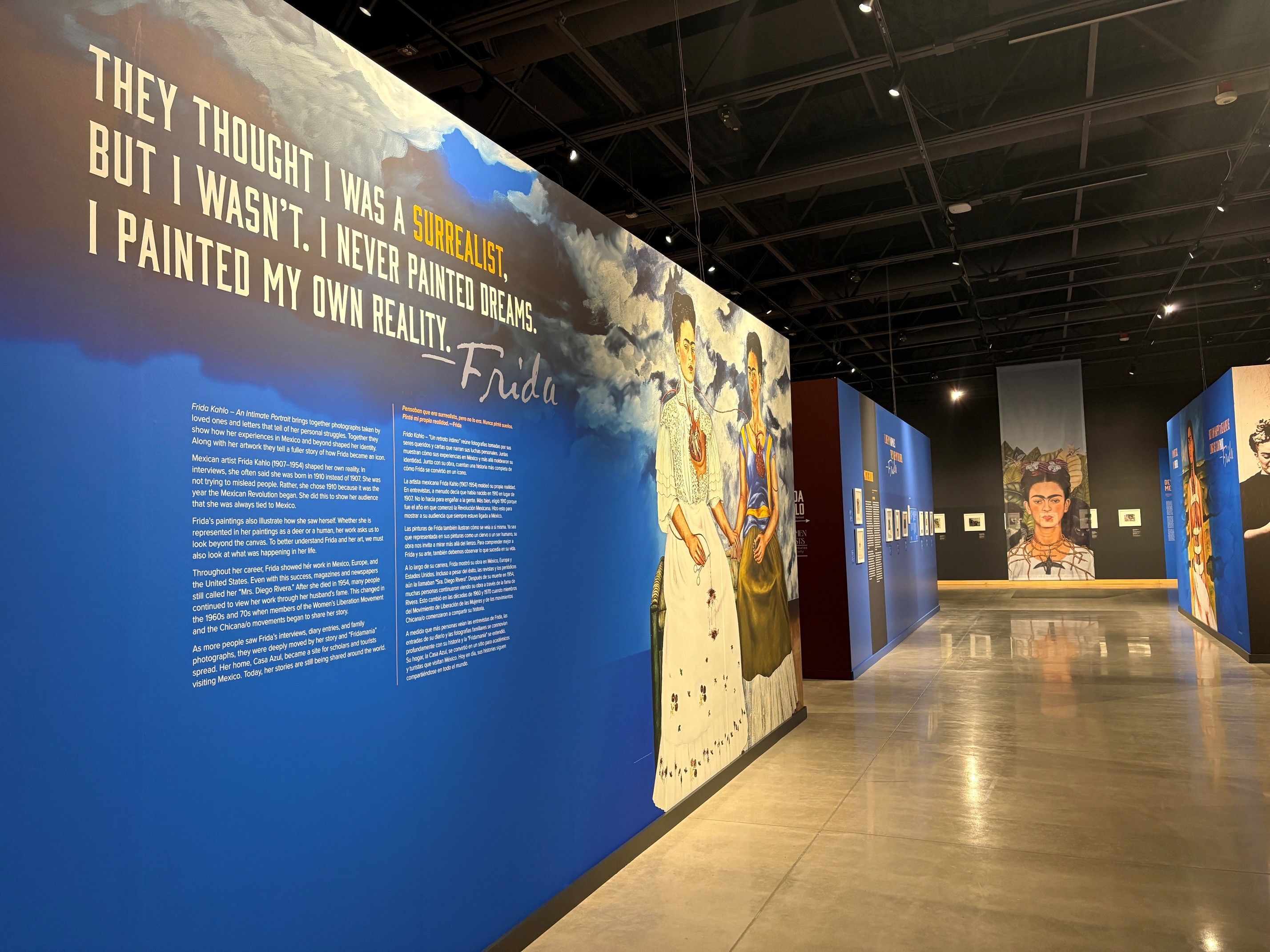 A gallery of a museum with a Frida Kahlo graphic along the wall