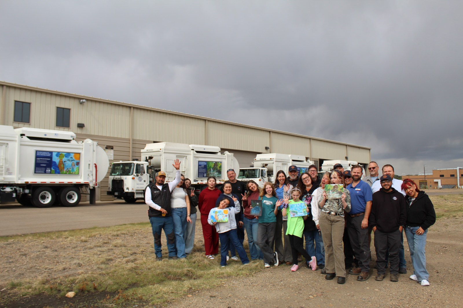 A group of people smiling and standing in front of several white truck featuring an artwork display.