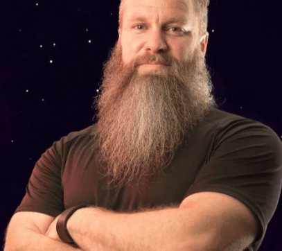 Head shot of a man with a beard and a black tee shirt against a black background.
