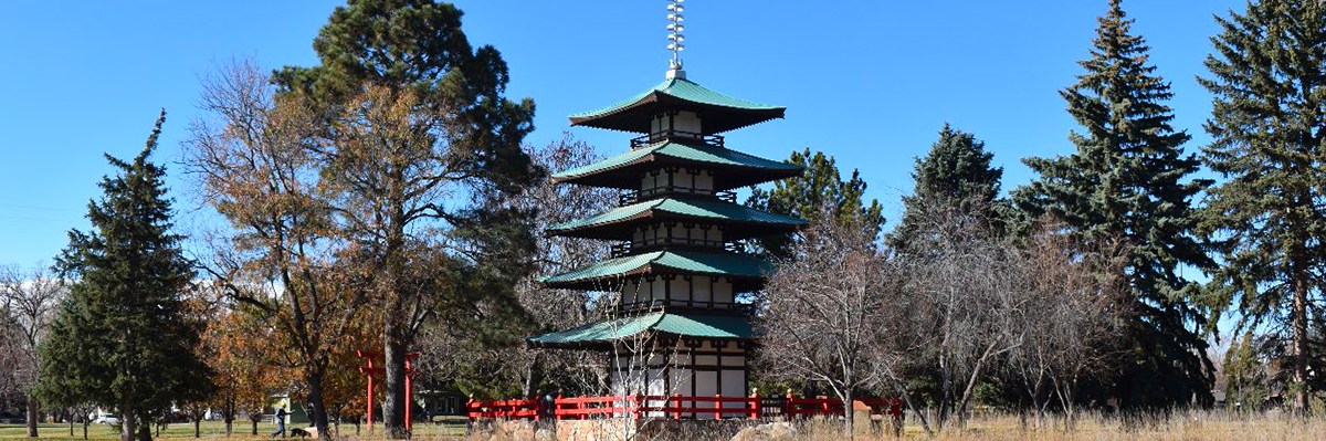 Located in Longmont Colorado's Kanemoto Park, the Tower of Compassion is a five-story pagoda. It has green roofs and is surrounded by a red fence and several tall trees.